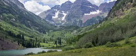 Maroon Bells peaks above a green mountain valley and lake near Aspen, Colorado