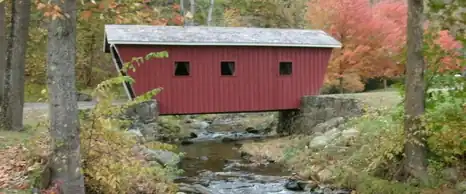 Red covered bridge over a rocky stream among autumn trees at Kent Falls State Park, Connecticut